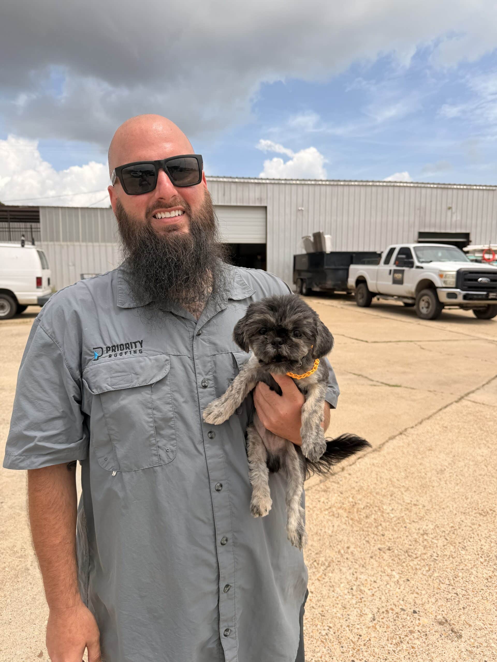 Roofing contractor holding a small dog outside the company shop.